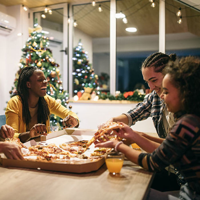  people around a table enjoying pizza together over the holidays
