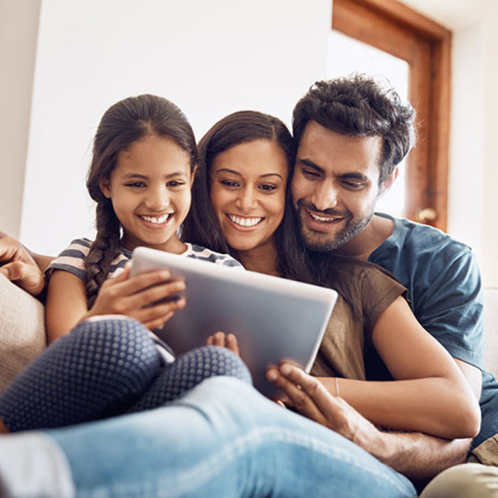 Mother, Father and Daughter on a couch looking at a tablet