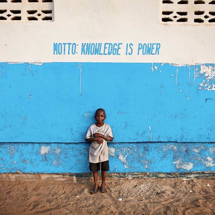 Young boy standing in front of building with the words Motto: Knowledge Is Power written on it